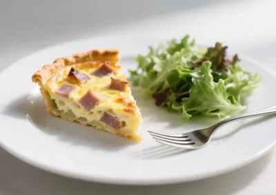 Tranche de quiche lorraine accompagnée d’une salade verte fraîche, dressée sur une assiette blanche.