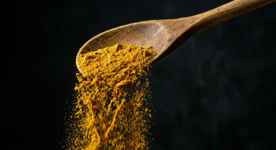 Gros plan sur une cuillère en bois versant du ras-el-hanout sur un fond sombre et minimaliste.