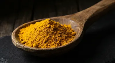 Gros plan d'une cuillère d'épice jaune vive sur fond sombre.