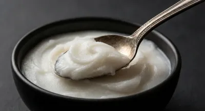 Gros plan d'une cuillère prélevant de la graisse de canard crémeuse sur fond sombre.